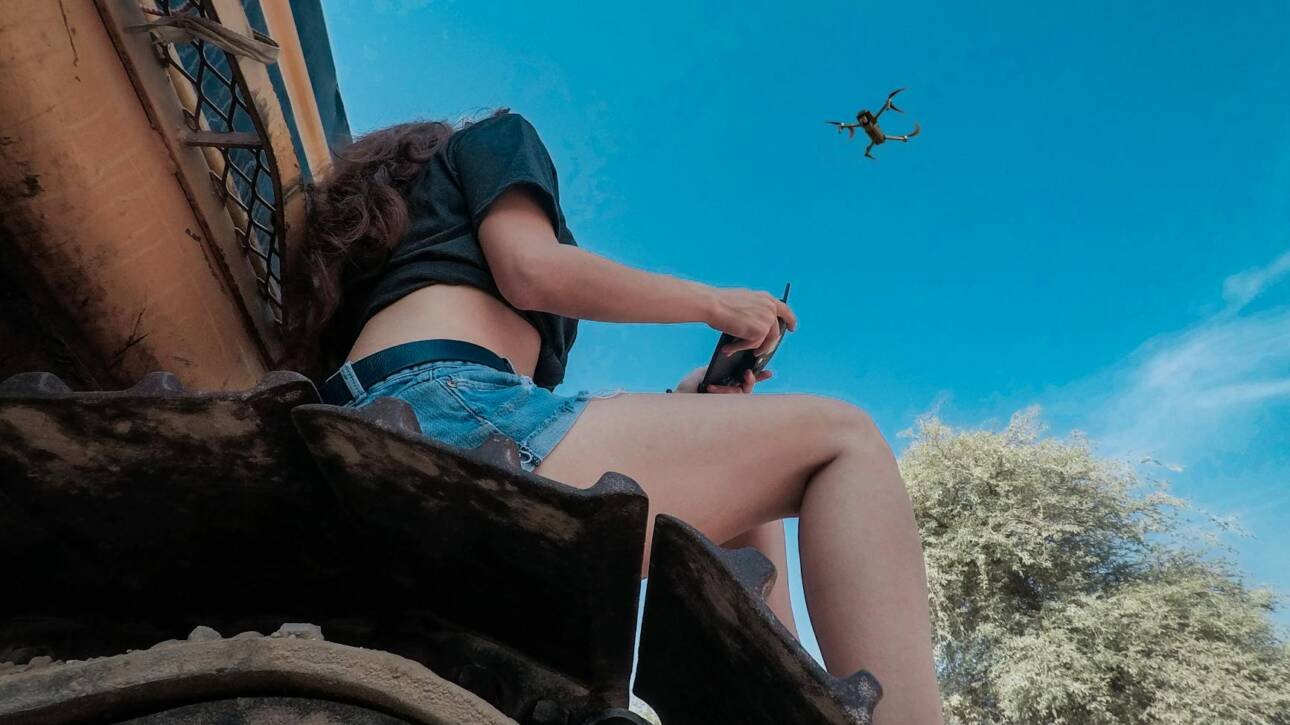 woman using black quadcopter drone while sitting on roof