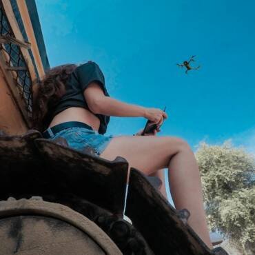 woman using black quadcopter drone while sitting on roof