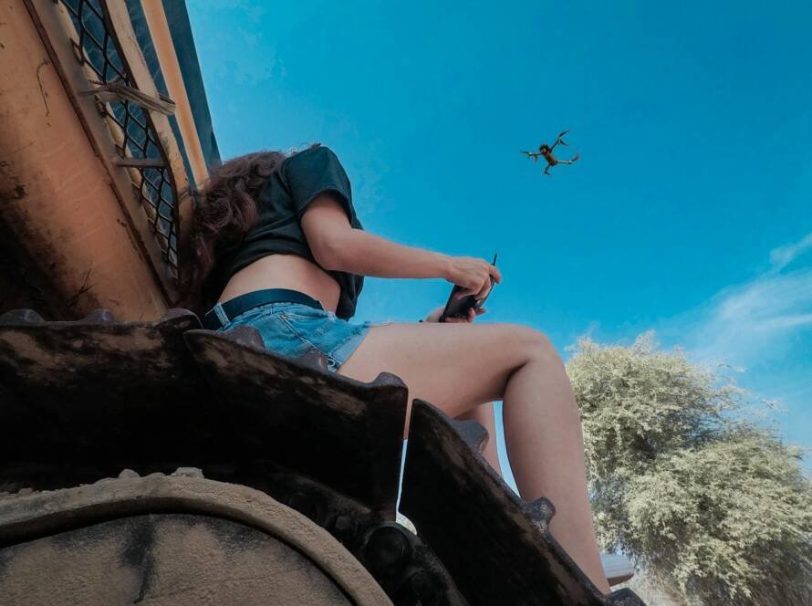 woman using black quadcopter drone while sitting on roof